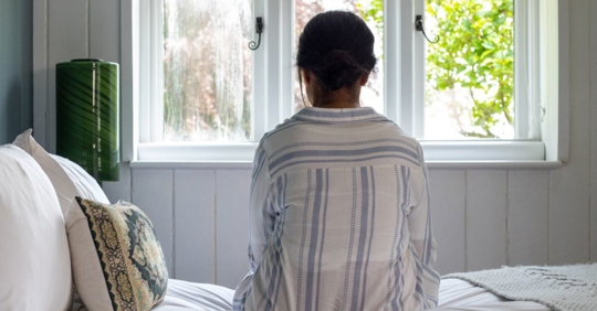 Back of woman as she stares out the window while on her bed
