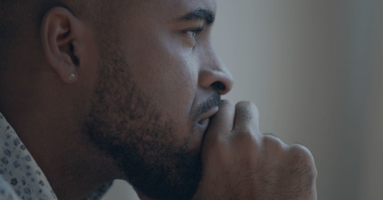 Side Profile of Young African American Man in Deep Throught with his hands to his chin and mouth