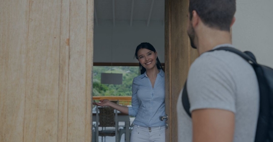 Young woman opening a door for a man gesturing for him to come inside.