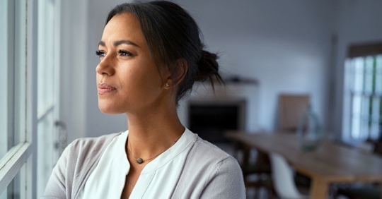 Young woman looking out of a window with pensive expression.