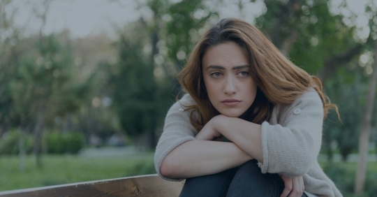 Young woman with sad expression and her knees up with her arms folded on top and chin resting on her arms.