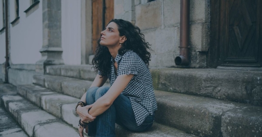 Side profile of a woman looking up and sitting on steps with her knees close to her chest and her arms wrapped around her knees.
