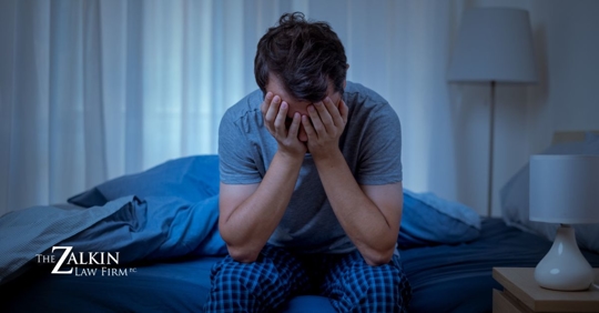 Man sitting on bed hunched over with his hands covering his face.