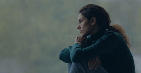 Woman staring out a window with a pensive expression.