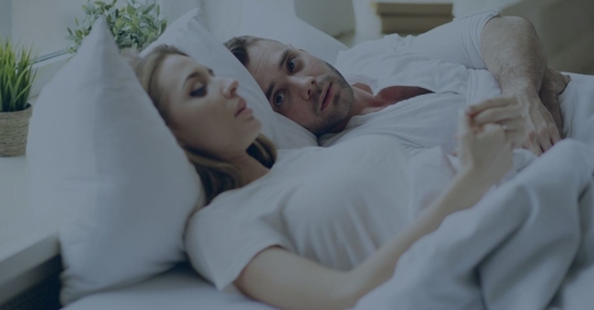 Man and woman laying in bed holding hands